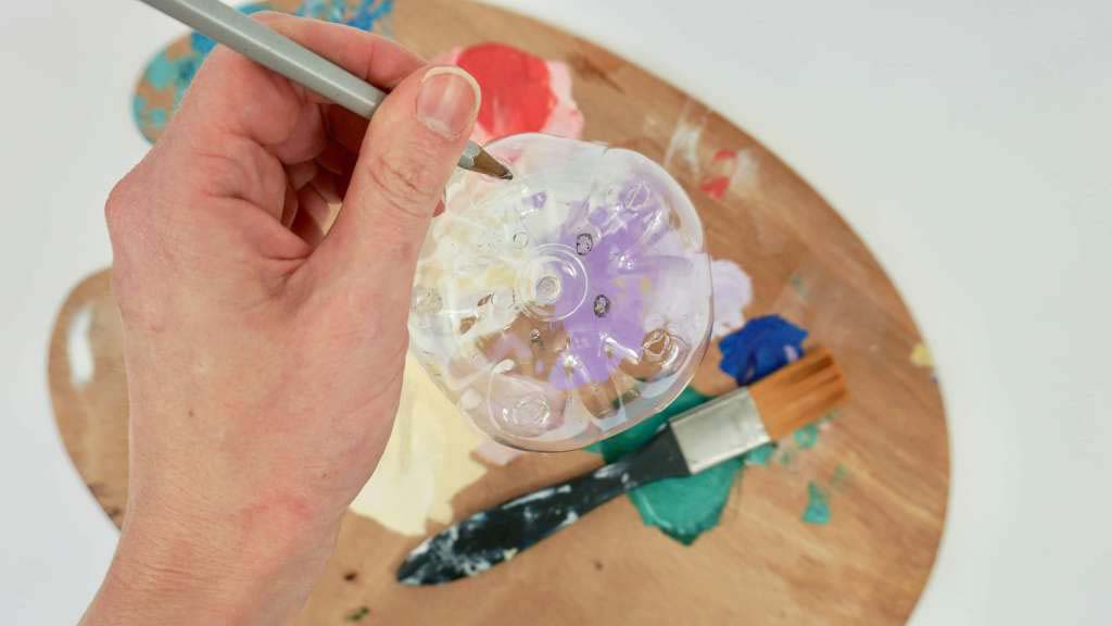 A close up of a hand holding a paintbrush over a water bottle on top of a paint palette. A close up of a hand holding a paintbrush over a water bottle on top of a paint palette.