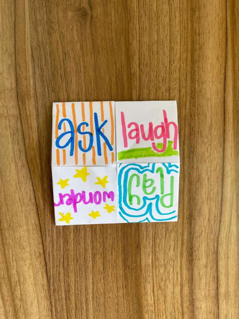 A piece of folded paper with the words ask, laugh, wonder, play. A piece of folded paper with the words ask, laugh, wonder, play.