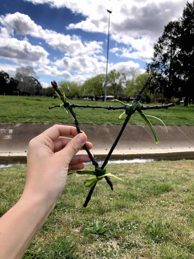 A close up of 4 sticks in the shape of a triangle held together by grass in the corners. A close up of 4 sticks in the shape of a triangle held together by grass in the corners.