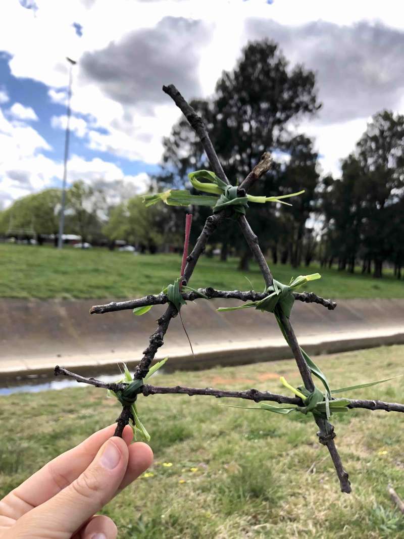 A close up of 4 sticks that look like a triangle held together by grass. It is the size of a hand. A close up of 4 sticks that look like a triangle held together by grass. It is the size of a hand.