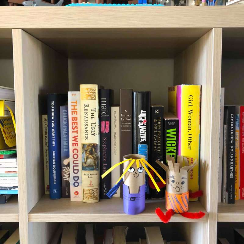 Two puppets made out of toilet rolls sit on a bookshelf. Two puppets made out of toilet rolls sit on a bookshelf.