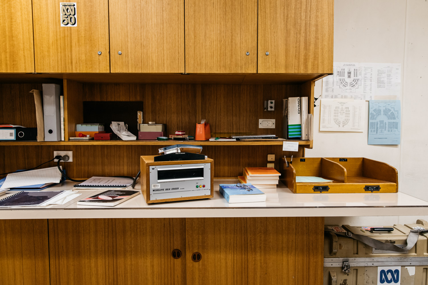 Brown old fashioned cupboard and desk with ABC stickers and the desktop covered in books, sticky tape and papers.