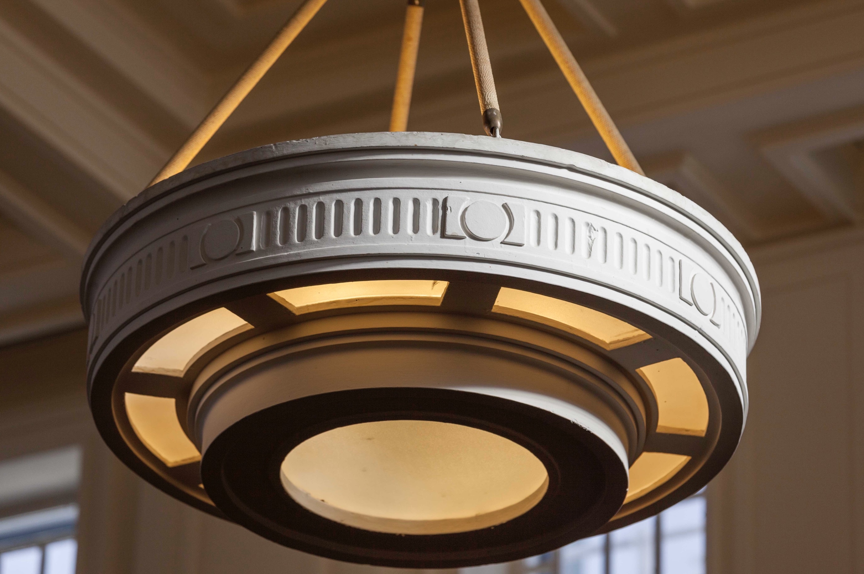 Square and circular motifs are features of the architecture and furniture throughout Old Parliament House. They appear on balcony rails, floor design, light fittings and the gold decoration on the glass doors. A close up detail shot of a pendant art-deco style light.