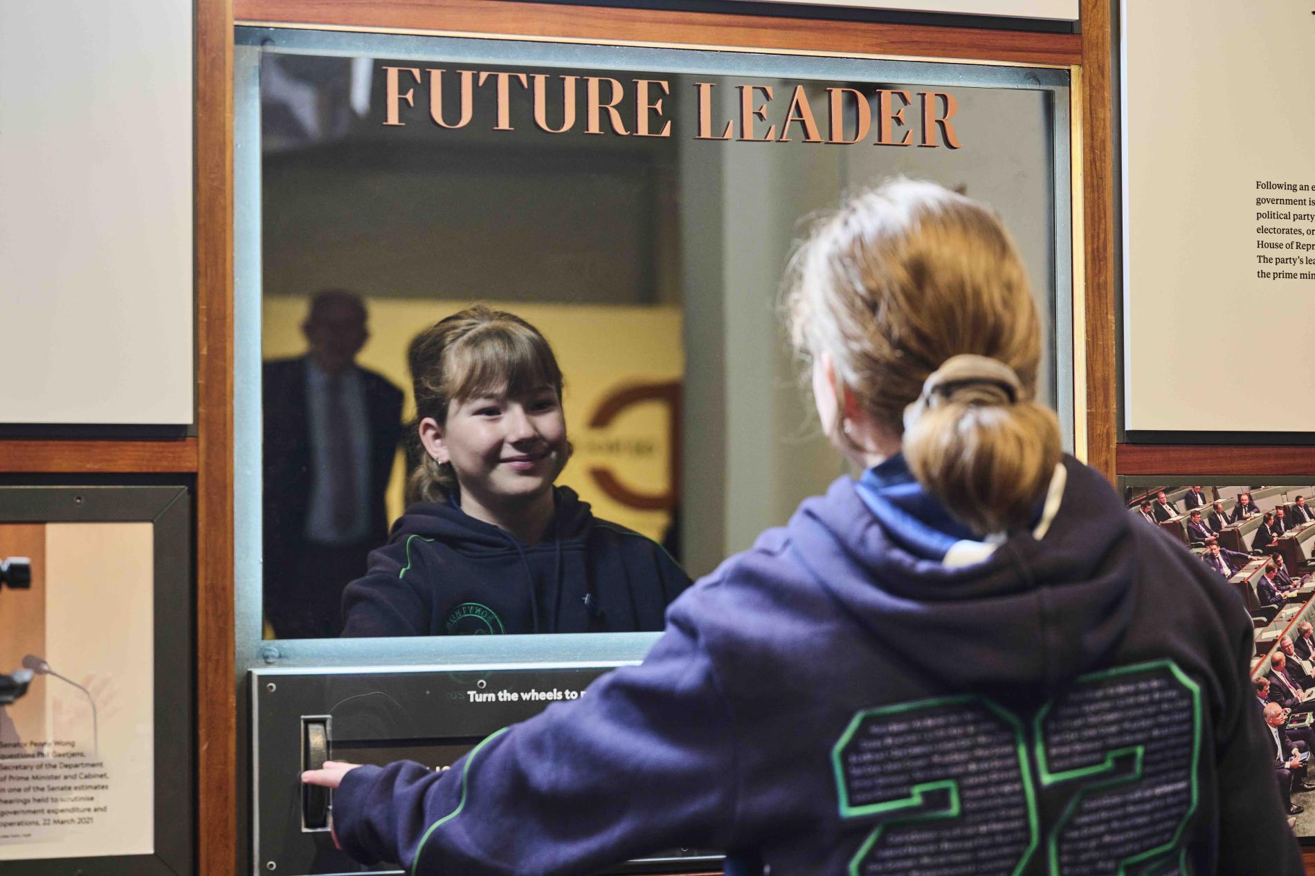 A primary school girl wearing her school jumper looks into a mirror with the words future leader on it. A primary school girl wearing her school jumper looks into a mirror with the words future leader on it.