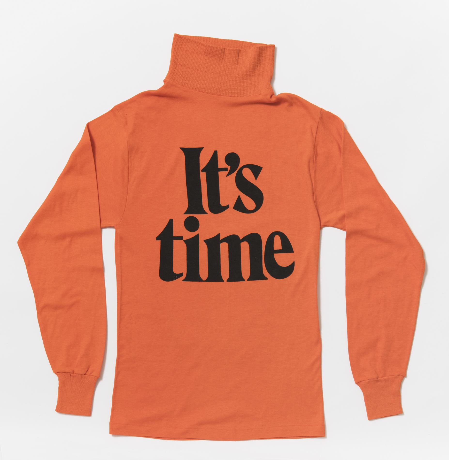 A bright orange long-sleeved skivvy with the words 'It's time' in big black font on the front. A bright orange long-sleeved skivvy with the words 'It's time' in big black font on the front.