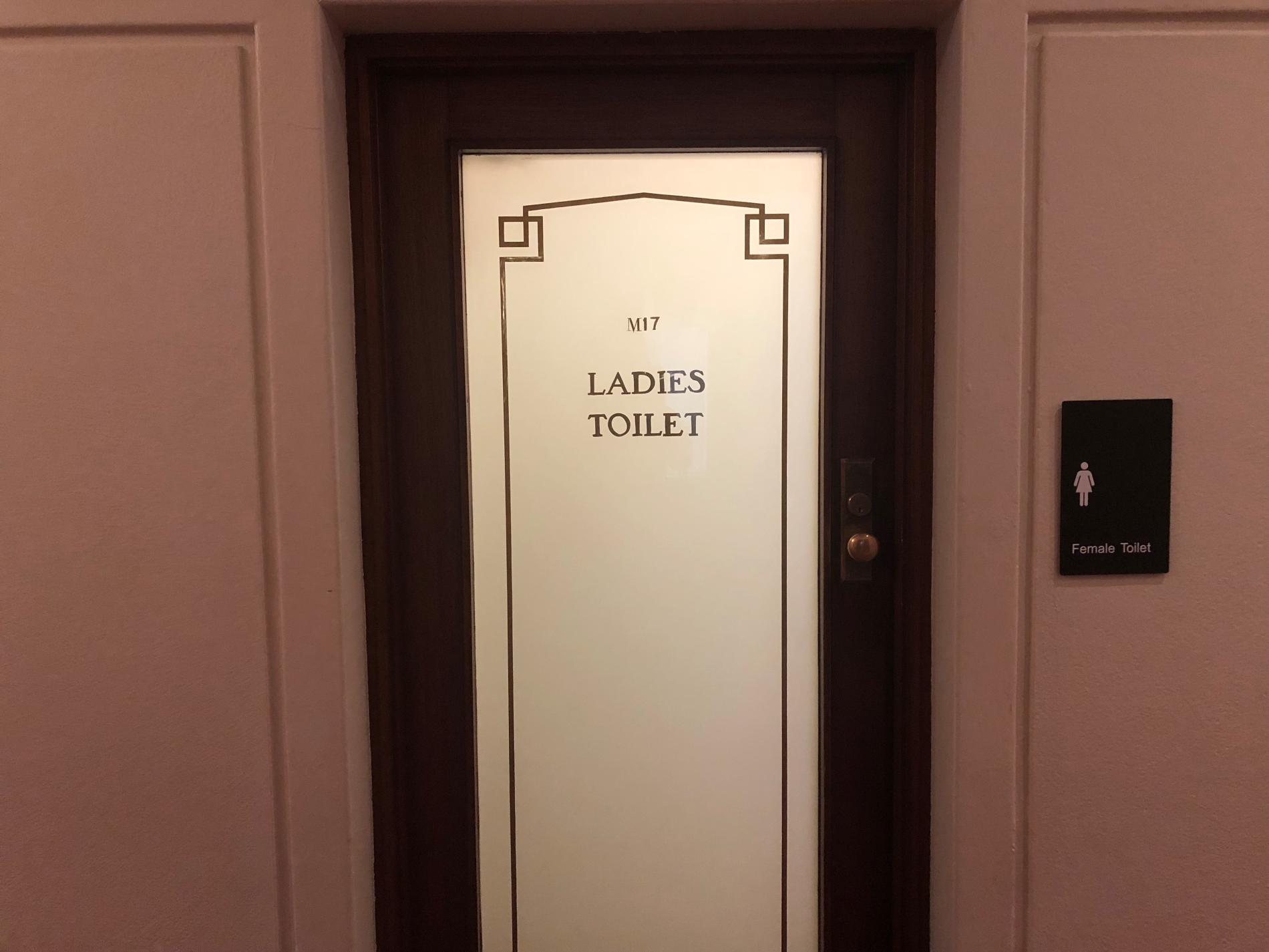 A wooden door with an ornate frosted glass panel with the words M17 Ladies Toilet. A wooden door with an ornate frosted glass panel with the words M17 Ladies Toilet.