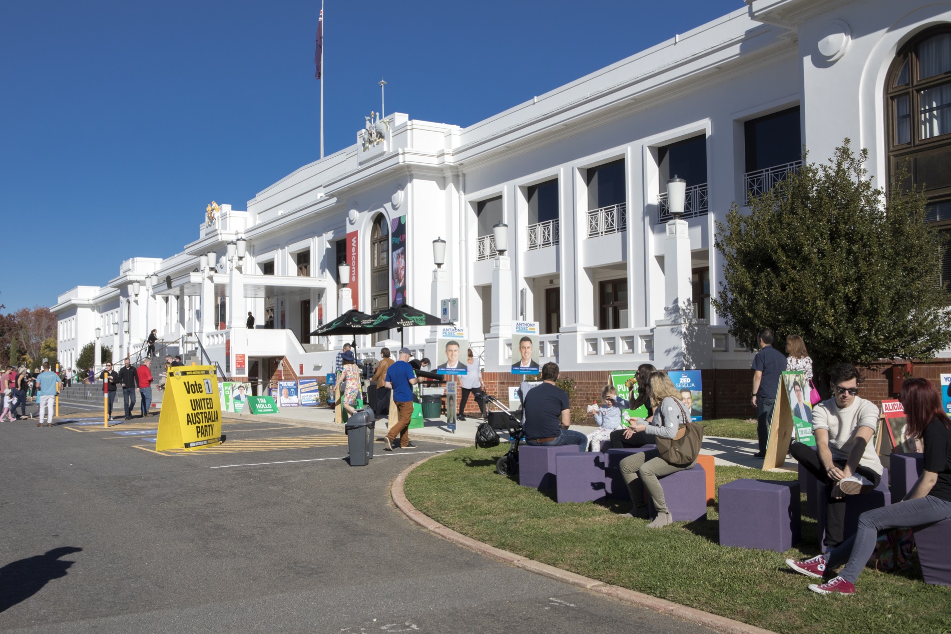 Many colourful signs and placards displaying political candidates, as people enter and leave Old Parliament House, with some sitting on purple blocks on the front lawn. Many colourful signs and placards displaying political candidates, as people enter and leave Old Parliament House, with some sitting on purple blocks on the front lawn.