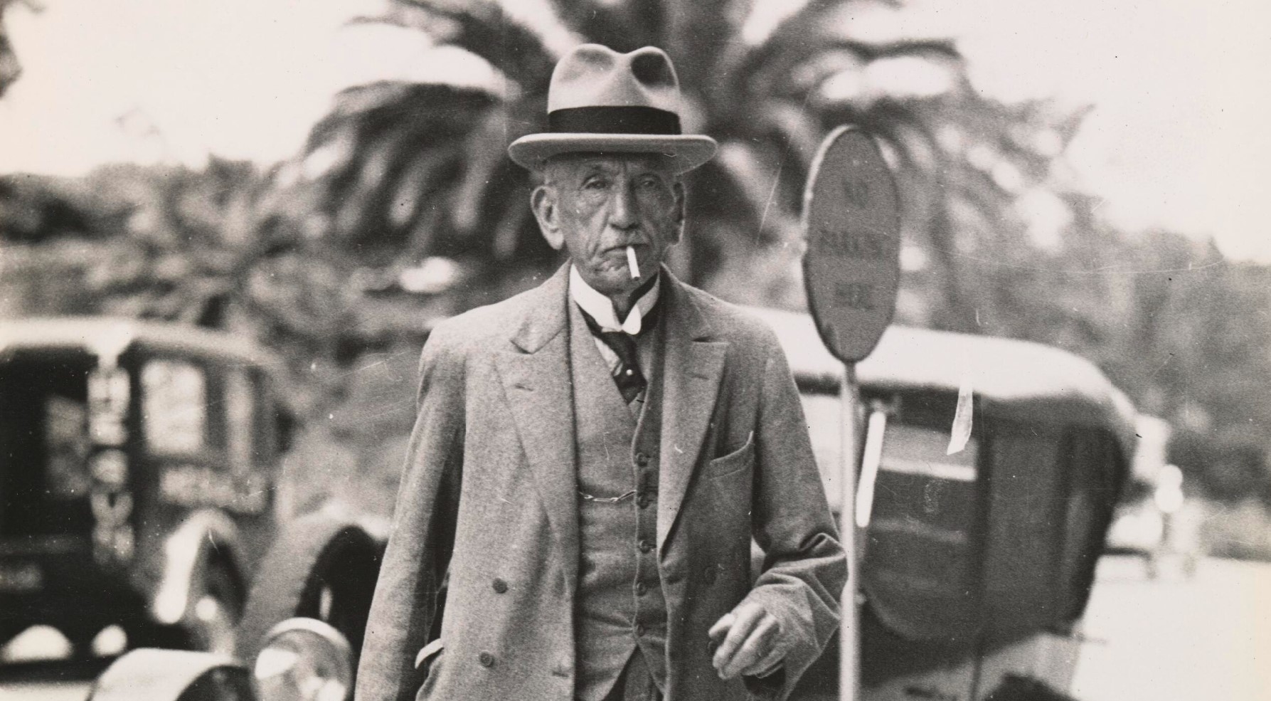Detail of William Hughes walks down the street wearing a hat and three-piece suit, smoking a cigarette. Detail of William Hughes walks down the street wearing a hat and three-piece suit, smoking a cigarette.