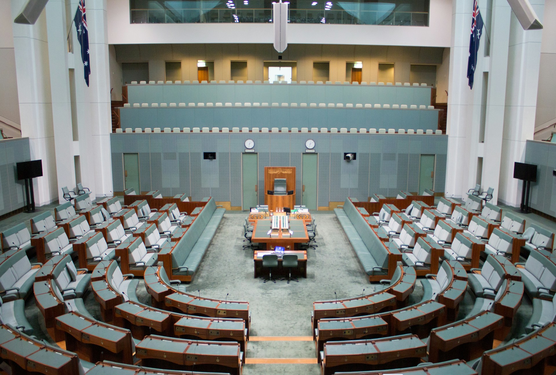 The House of Representatives, a room with grey-green furnishings, with benches arranged in a horse-shoe shape around a central long bench and chair. The House of Representatives, a room with grey-green furnishings, with benches arranged in a horse-shoe shape around a central long bench and chair.