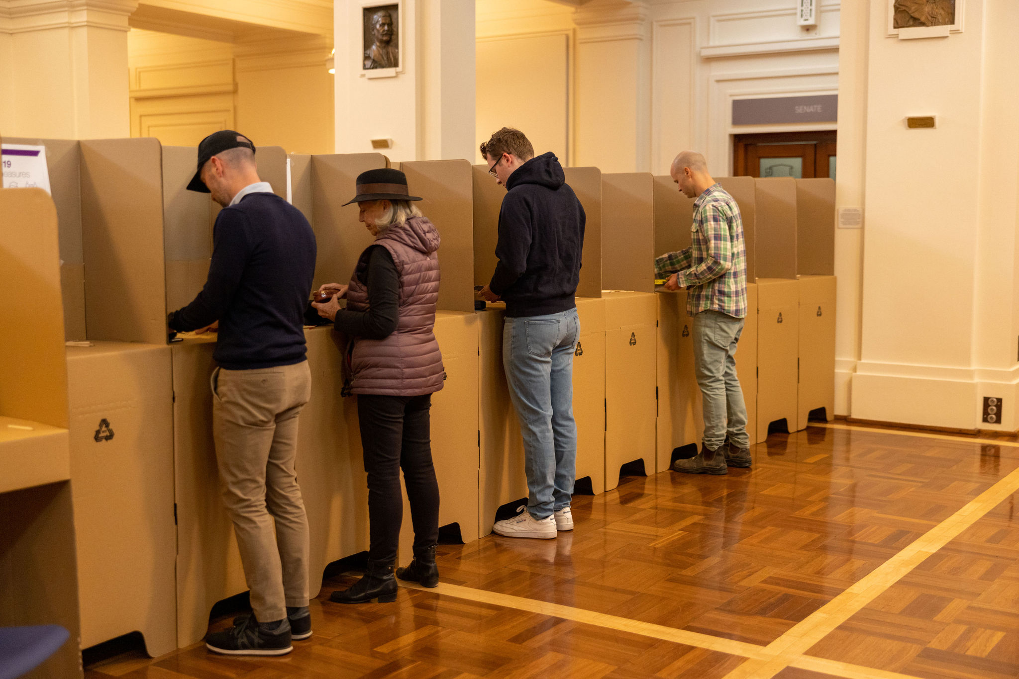 Four people, three men and a woman, standing at cardboard election booths in King's Hall. Four people, three men and a woman, standing at cardboard election booths in King's Hall.