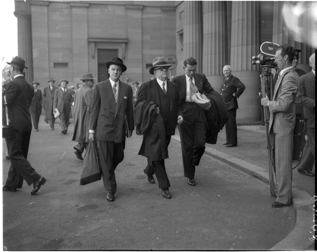 Dr Evatt is flanked by two assistants as he enters the Petrov Royal Commission in Darlinghurst. Men are walking nearby, with a man standing with a camera recording them. Dr Evatt is flanked by two assistants as he enters the Petrov Royal Commission in Darlinghurst. Men are walking nearby, with a man standing with a camera recording them.