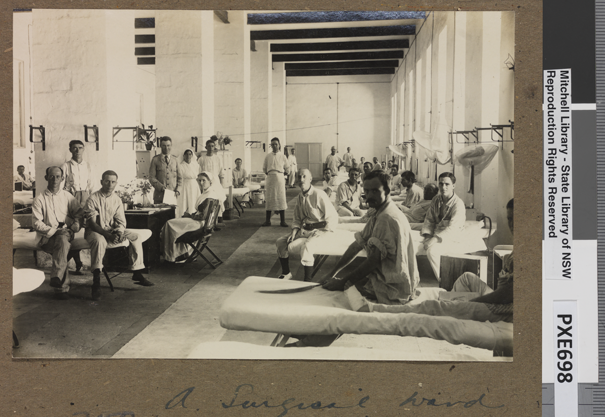 A surgical ward in Egypt during WWII with rows of beds with men looking at the camera. Earle Page is standing holding a piece of paper, next to a nurse. A surgical ward in Egypt during WWII with rows of beds with men looking at the camera. Earle Page is standing holding a piece of paper, next to a nurse.