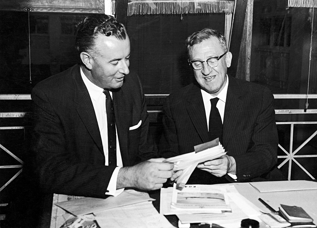 Arthur Calwell and Gough Whitlam are both holding and looking at some papers. Arthur Calwell and Gough Whitlam are both holding and looking at some papers.