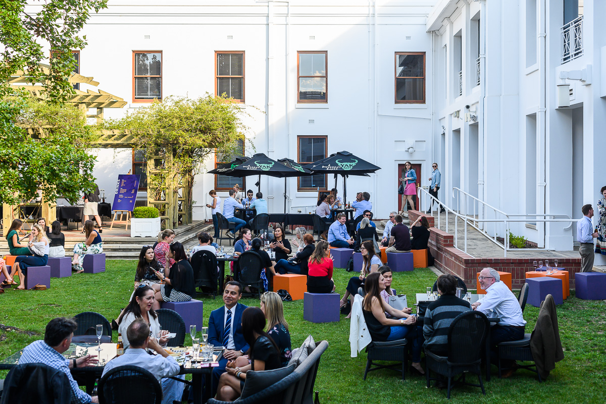 People sit at tables and on stools in the Old Parliament House courtyard having drinks.