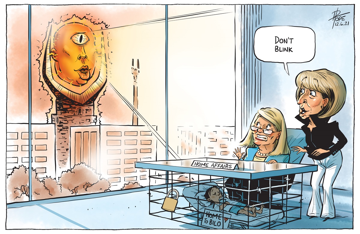 Michaelia Cash says, 'Don't blink' to Karen Andrews. Underneath Andrews' 'Home Affairs' desk a sick child is locked in a cage. Peter Dutton depicted with one eye is outside watching.