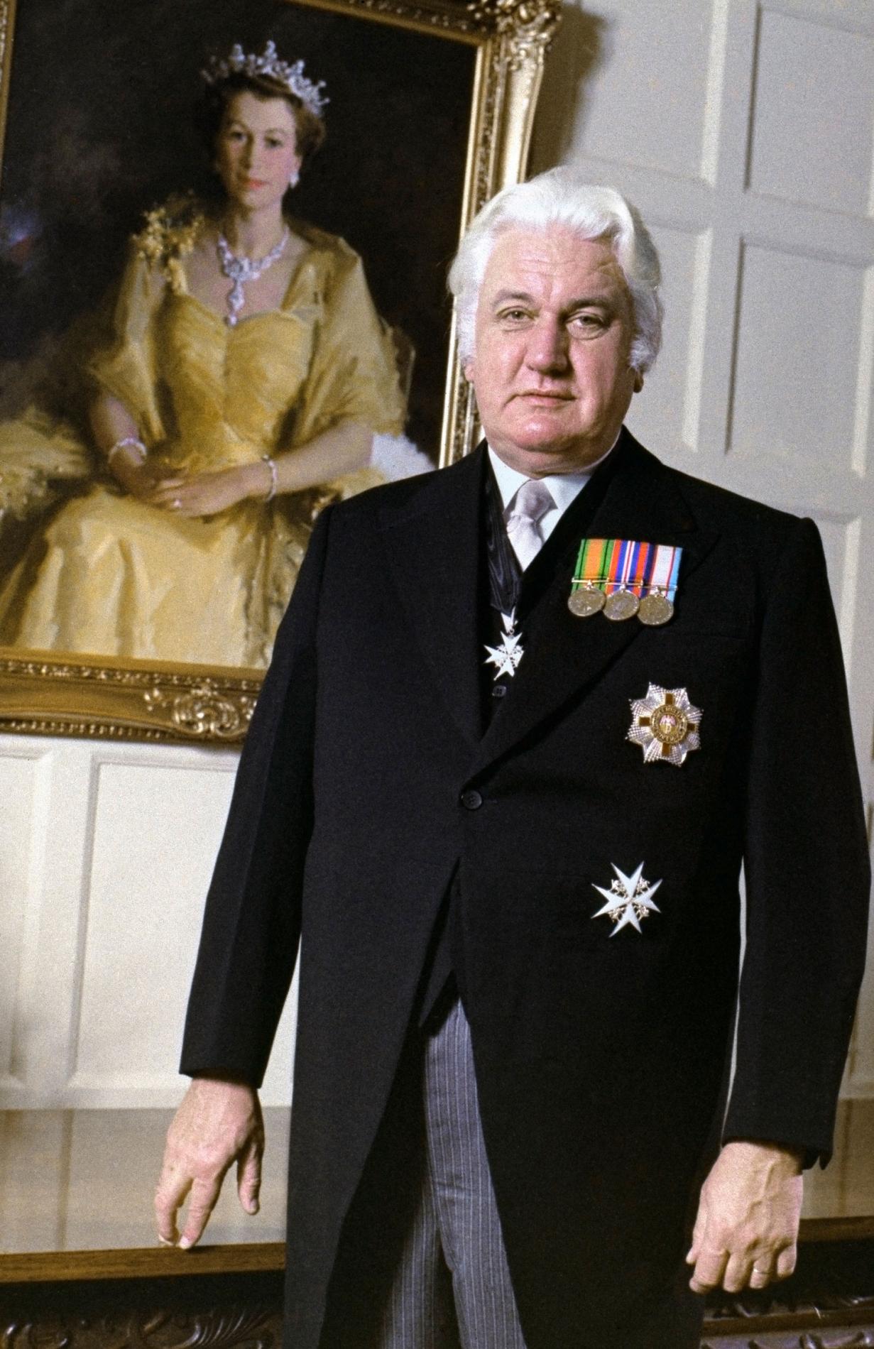 Sir John Kerr dressed in a morning suit stands in front of an oil painting of Queen Elizabeth II. Sir John Kerr dressed in a morning suit stands in front of an oil painting of Queen Elizabeth II.