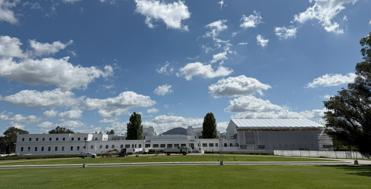 A view of the back of Old Parliament House, a long white building with a white scaffolding over one section of the roof and walls. 