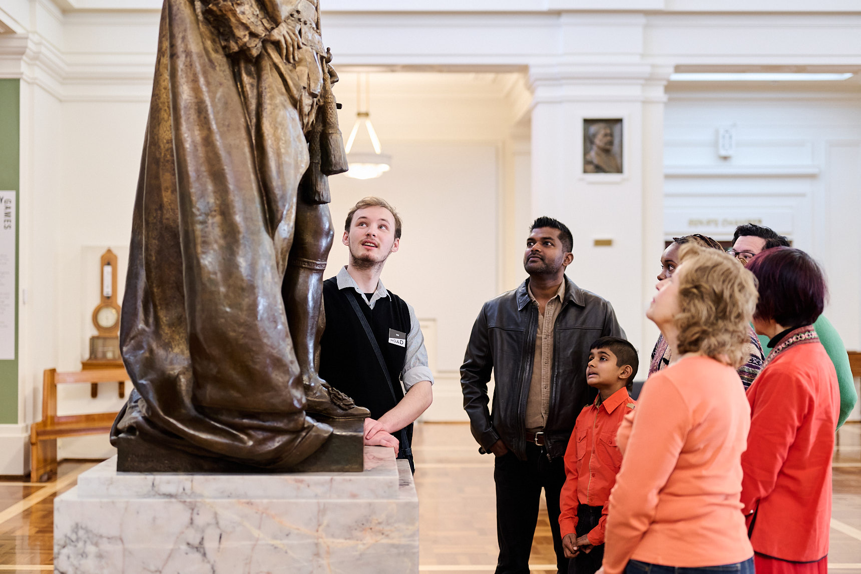 People stand in a group in King's Hall in Old Parliament House looking at a bronze statue of King George.