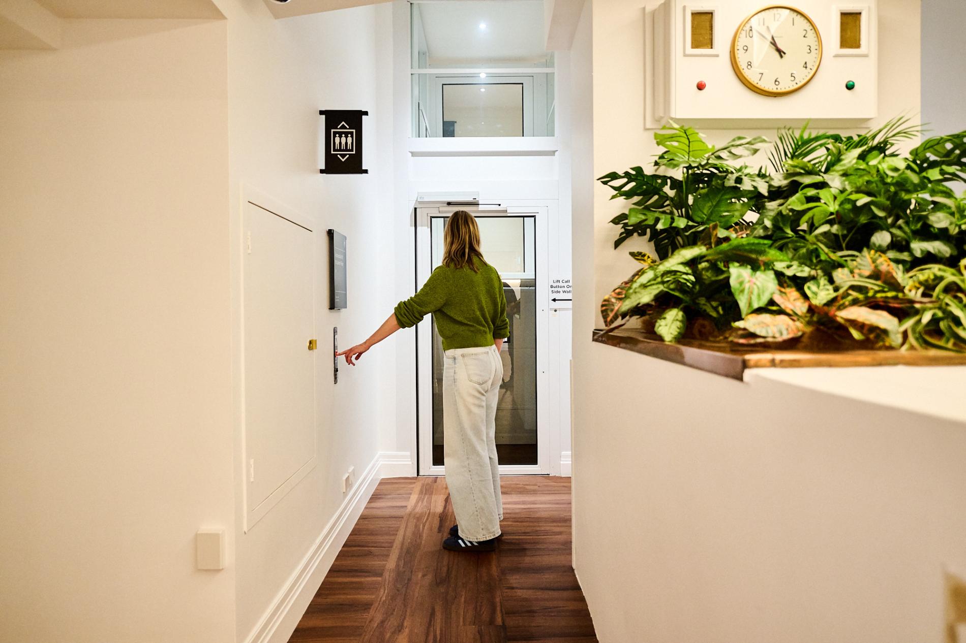 A woman in a green sweater presses the call button for an accessible lift in Old Parliament House.