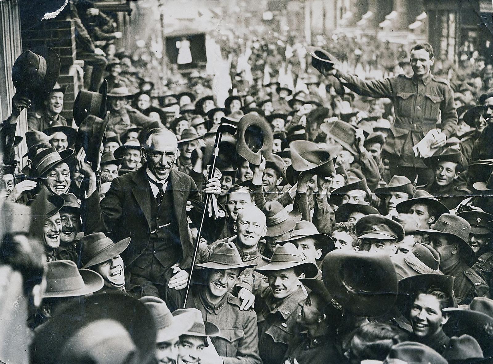 Prime Minister Billy Hughes is carried by soliders through a crowded street.