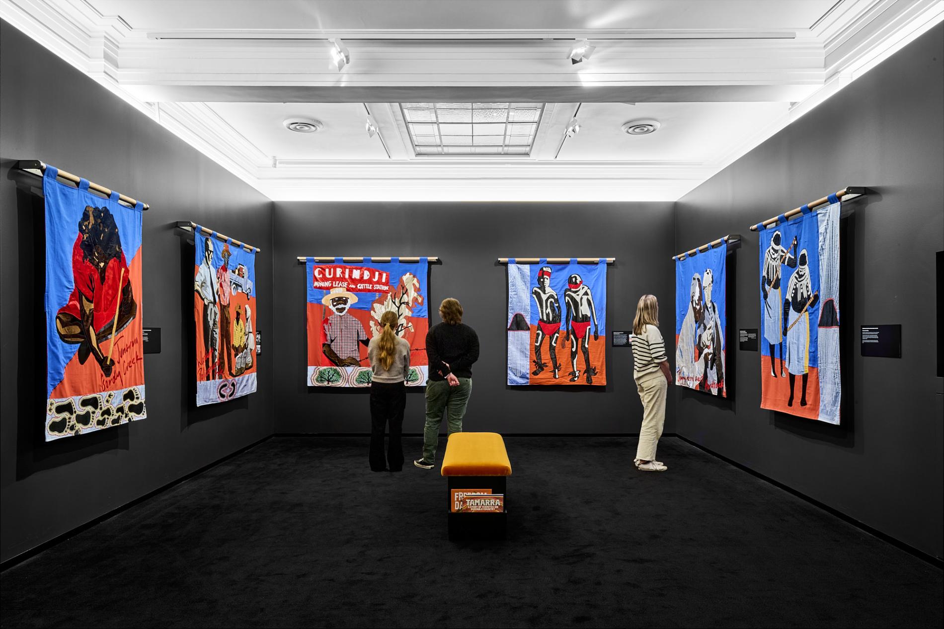 Three people stand looking at the Gurindji freedom banners exhibition in Old Parliament House.