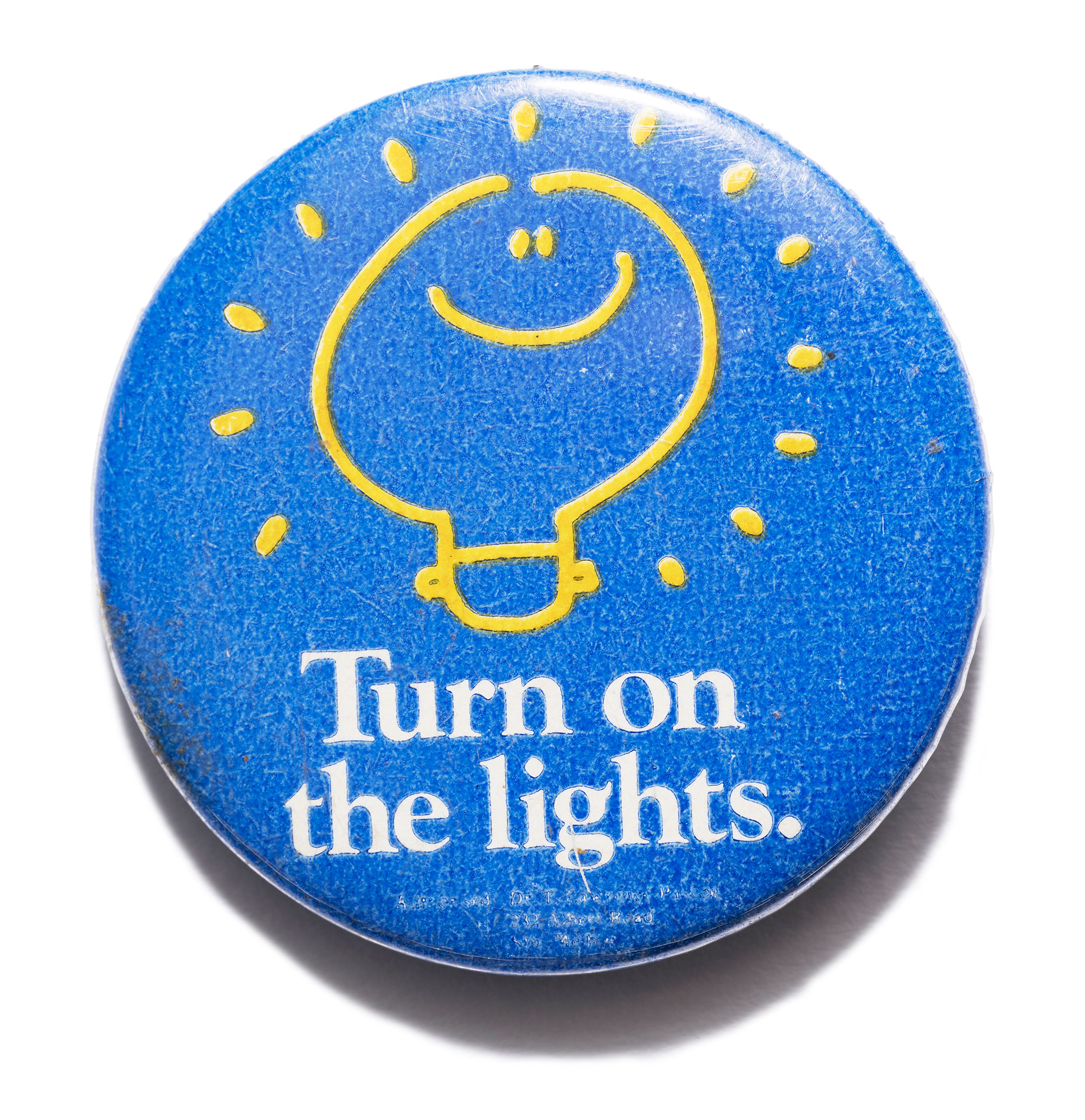 A blue badge with white text and a yellow lightbulb with a smiley face. Text reads, 'Turn on the lights'.