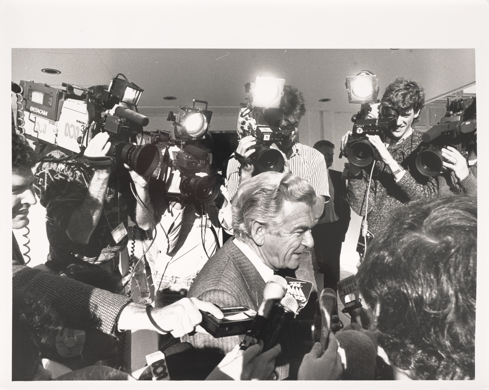 Prime Minister Bob Hawke arriving at Parliament House being swarmed by the media, all pointing cameras in his face.