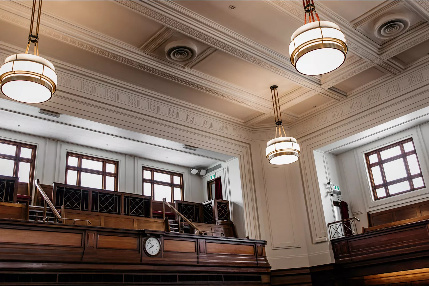 A close up of a white ceiling with ornate detailing, art-deco style pendant lighting and a timber gallery for the press to look down onto the floor of the House of Representatives. A close up of a white ceiling with ornate detailing, art-deco style pendant lighting and a timber gallery for the press to look down onto the floor of the House of Representatives.