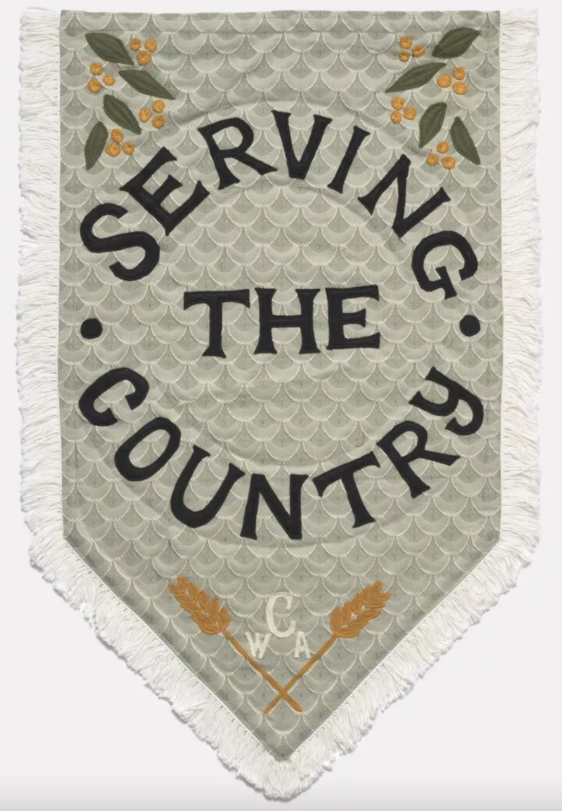 Soft green coloured tapestry with wattle and leaf motif on the left and right top corners. Underneath are the words 'Serving the country' and below that the acronym for the Country Women's Association, 'CWA'. Soft green coloured tapestry with wattle and leaf motif on the left and right top corners. Underneath are the words 'Serving the country' and below that the acronym for the Country Women's Association, 'CWA'.