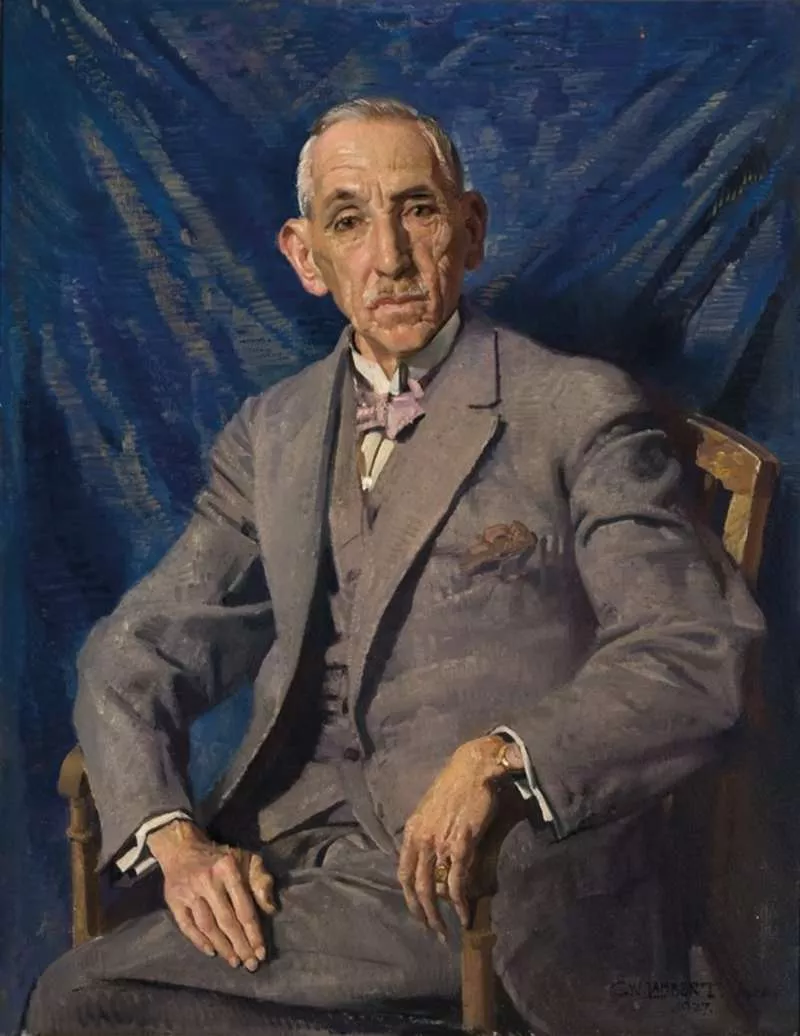 Former prime minister Billy Hughes in a grey suit, with a pink bowtie, sitting in a wood chair in front of a dark blue curtain. Former prime minister Billy Hughes in a grey suit, with a pink bowtie, sitting in a wood chair in front of a dark blue curtain.
