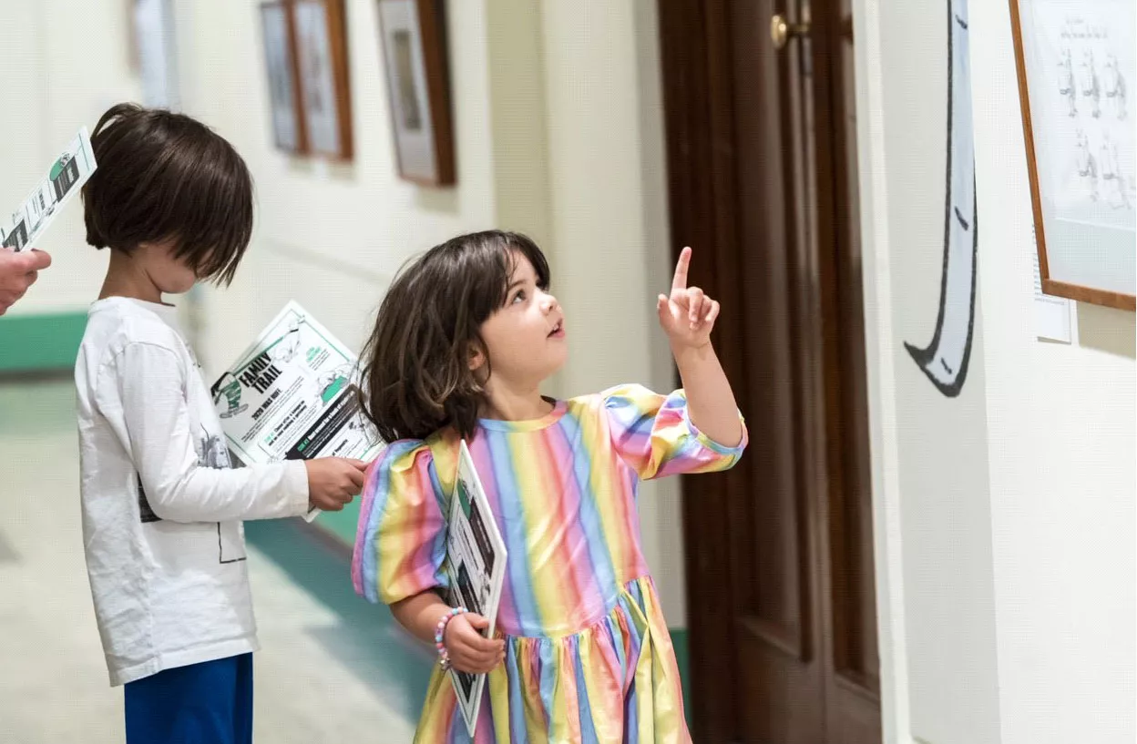 A young girl in a striped dress pointing to a Behind the Lines cartoon A young girl in a striped dress pointing to a Behind the Lines cartoon