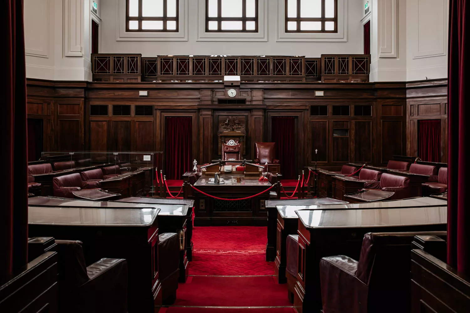 Two small steps with red carpet leading into the Senate Chamber with dark wooden furniture positioned in U-shape around a central table. Two small steps with red carpet leading into the Senate Chamber with dark wooden furniture positioned in U-shape around a central table.