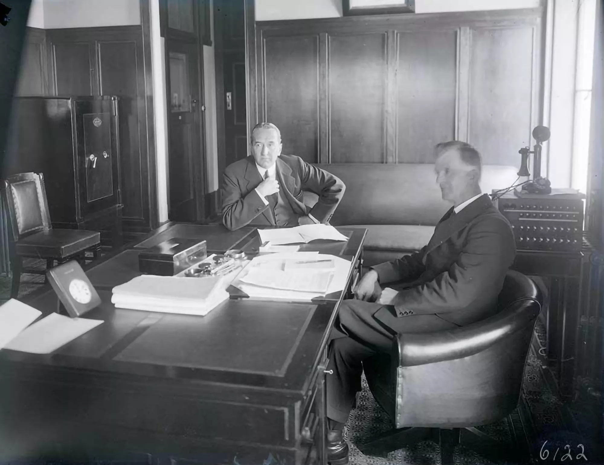 Two men in suits, Stanley Bruce and James Scullin, sit at a large wooden desk. Two men in suits, Stanley Bruce and James Scullin, sit at a large wooden desk.
