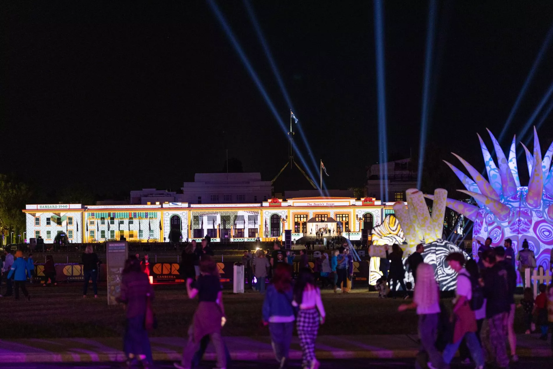 A night shot of Old Parliament House, a large white long building, with people gathering out the front and coloured lights projected onto the surface. A night shot of Old Parliament House, a large white long building, with people gathering out the front and coloured lights projected onto the surface.