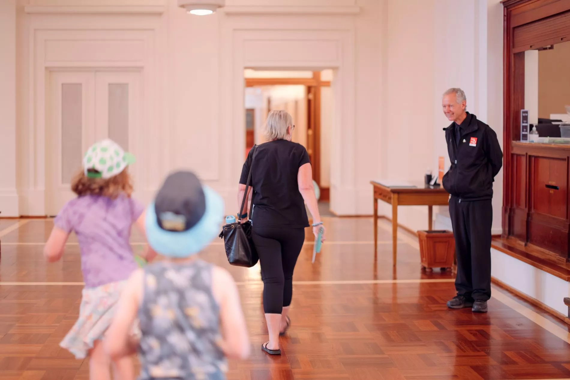 A woman and two children walk towards a museum experience officer dressed in a black uniform with a MoAD badge. A woman and two children walk towards a museum experience officer dressed in a black uniform with a MoAD badge.