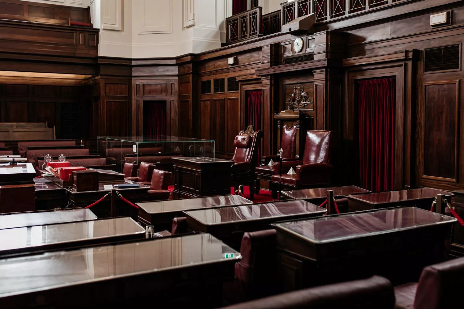A room with rows of glass topped benches facing a red leather chair, with red curtins and timber panelling. A room with rows of glass topped benches facing a red leather chair, with red curtins and timber panelling.