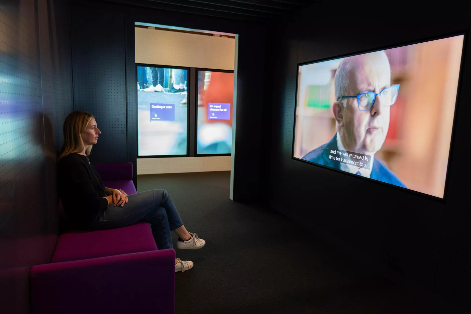 A woman is sitting and viewing a large screen in an exhibition. A woman is sitting and viewing a large screen in an exhibition.