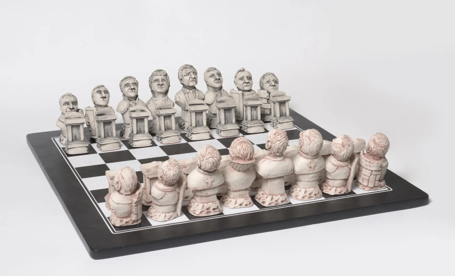 A chess set featuring politicians carved from a stone. The faces of the black chess pieces are visible and the backs of the white pieces. A chess set featuring politicians carved from a stone. The faces of the black chess pieces are visible and the backs of the white pieces.