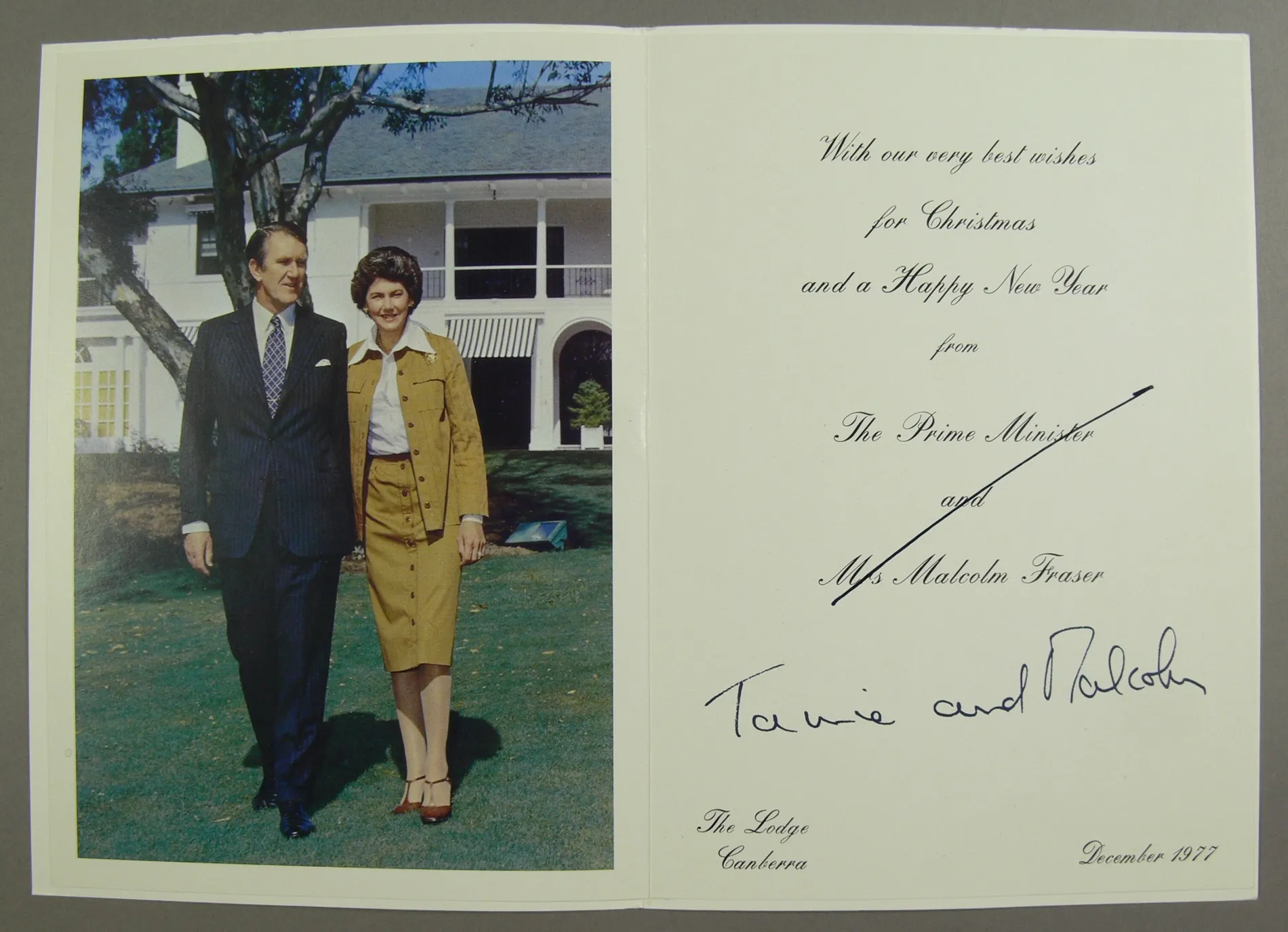 A Christmas card featuring a photo of Malcolm Fraser wearing a dark blue pinstripe suit and Tamie Fraser wearing a tan safari suit and white blouse, posing in front of their home. A Christmas card featuring a photo of Malcolm Fraser wearing a dark blue pinstripe suit and Tamie Fraser wearing a tan safari suit and white blouse, posing in front of their home.