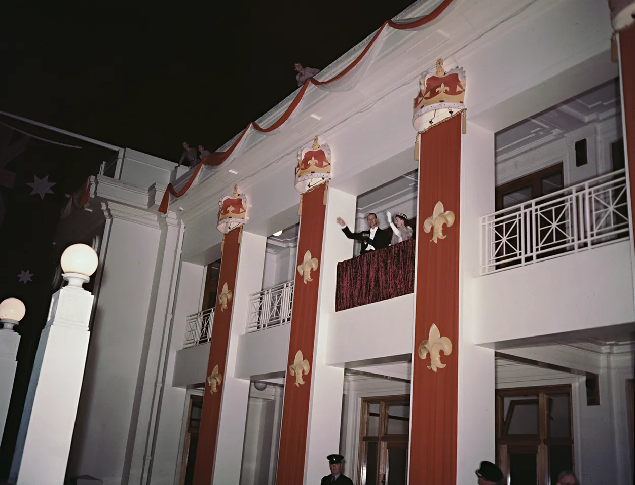Prince Phillip and the Queen wave to a crowd from a balcony at Parliament House. It is at night. Prince Phillip and the Queen wave to a crowd from a balcony at Parliament House. It is at night.