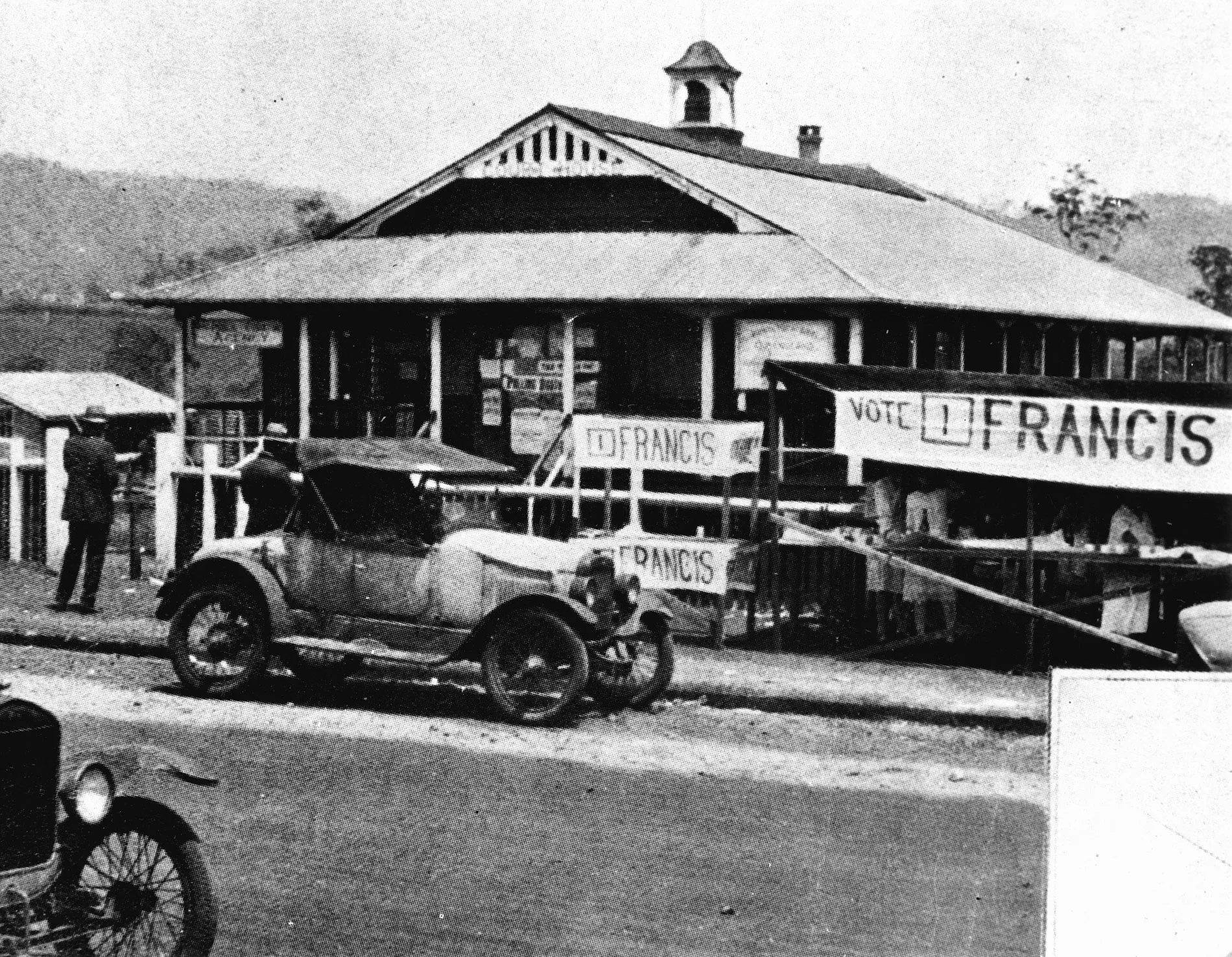 An old fashioned car on a street outside the old Atherton Courthouse in Queensland in 1928. Banners out the front read '1 Francis'. Women sell refreshments out the front at a stall. An old fashioned car on a street outside the old Atherton Courthouse in Queensland in 1928. Banners out the front read '1 Francis'. Women sell refreshments out the front at a stall.