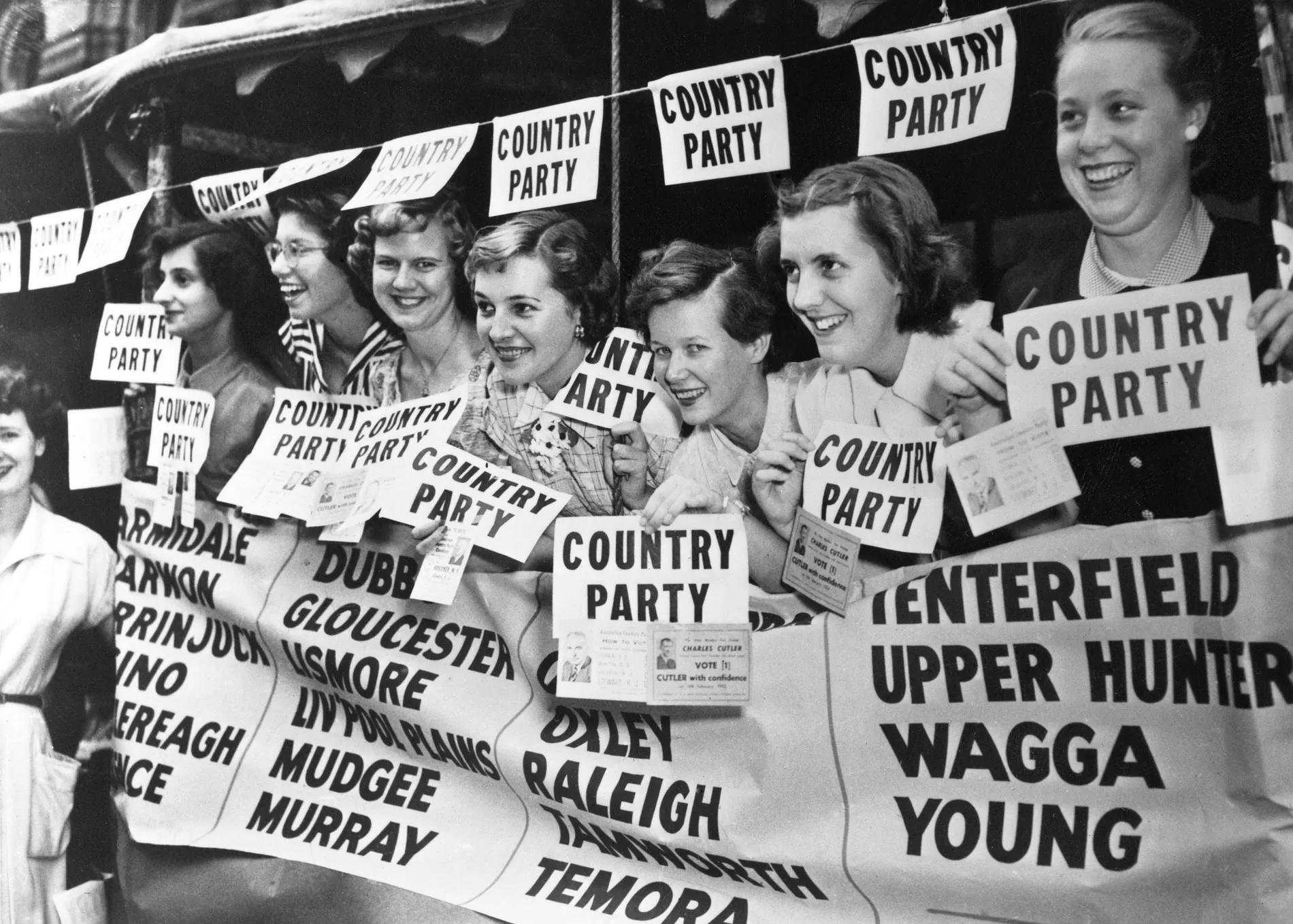 Women hold Country Party flyers for the 1968 election. They are in booth covered in campaign material.