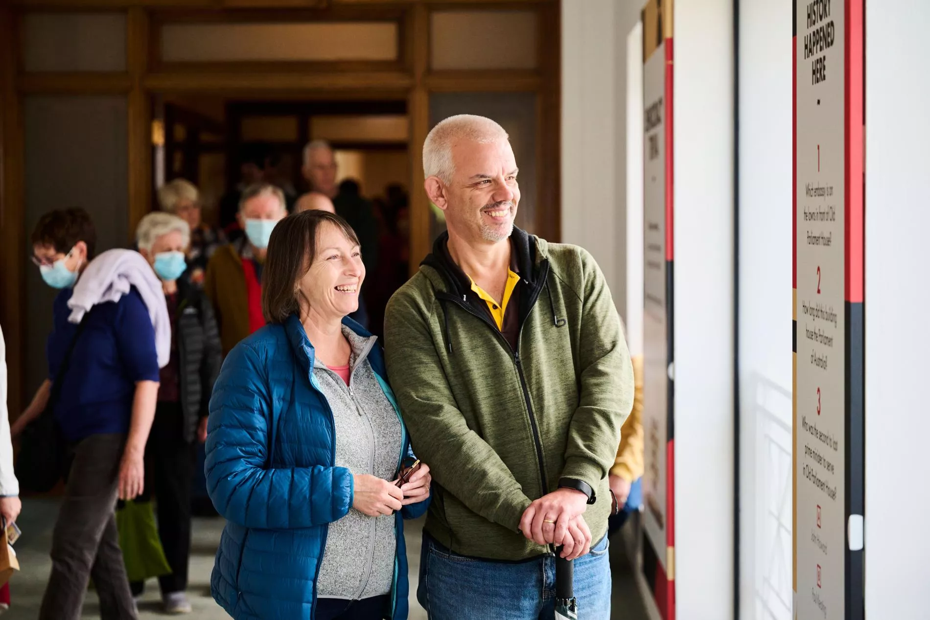 A man and a woman visiting a museum look up at a sign and read it while smiling.