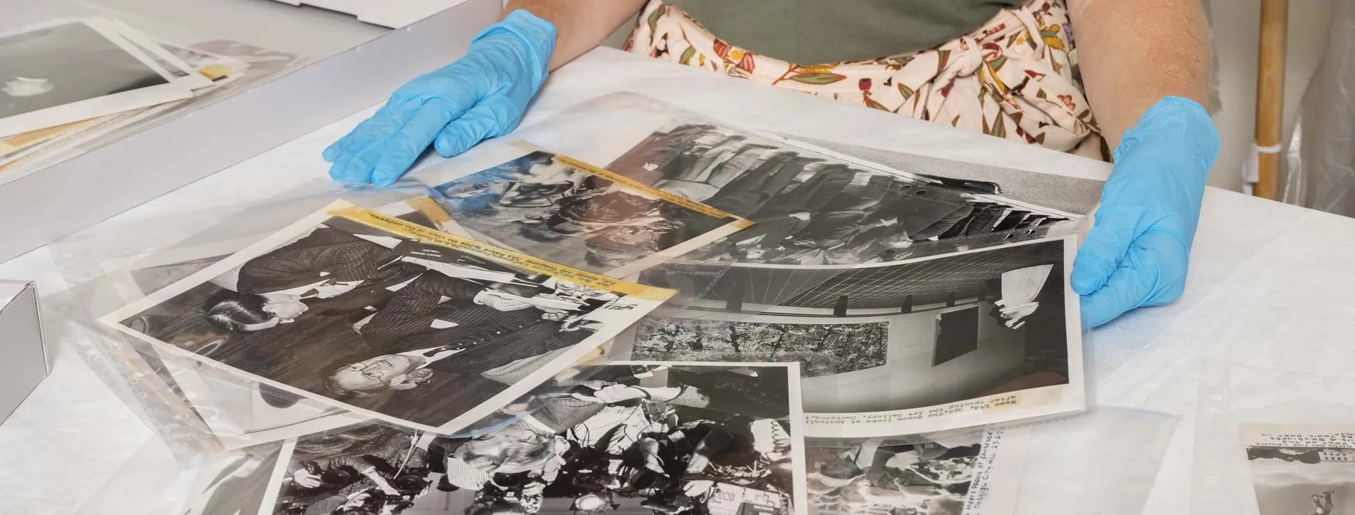 A person wearing blue gloves sorts black and white photographs on a desk. 