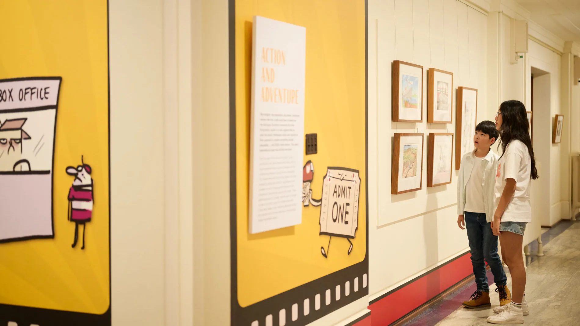 Two kids look at a wall of political cartoons in Old Parliament House.