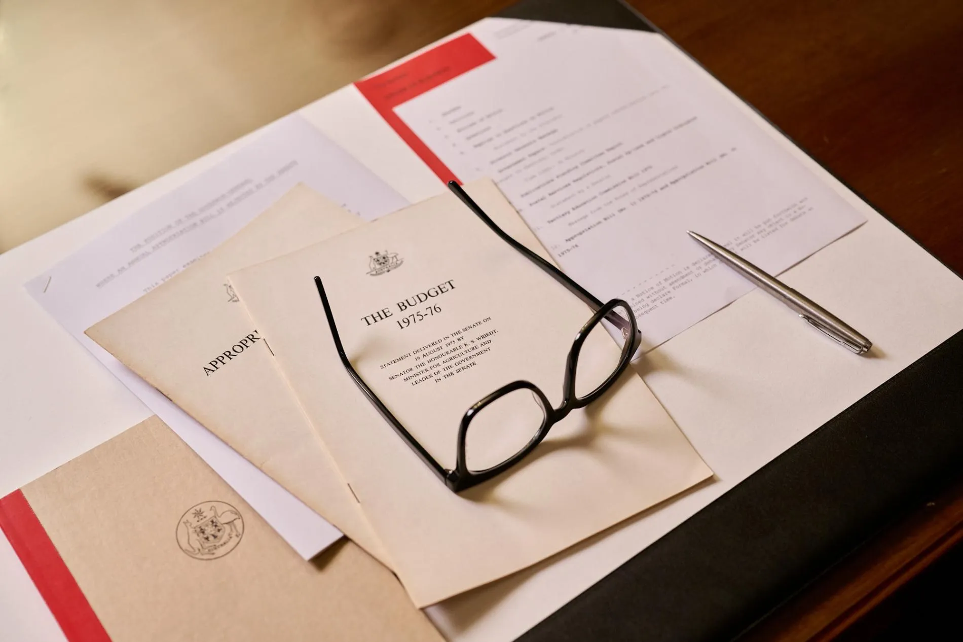 A pair of glasses rest of documents including one titled, 'The Budget 1975-76'. A pair of glasses rest of documents including one titled, 'The Budget 1975-76'.