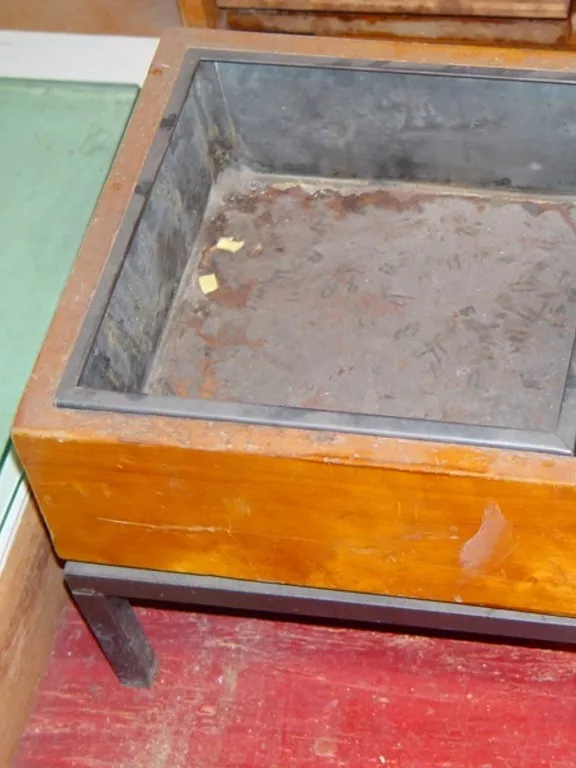 Wooden floor ashtray with a metal insert. A square wooden ashtray with a metal insert and sitting on a metal base with four small legs.