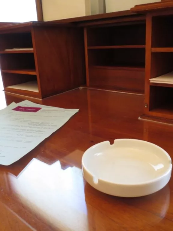 White ceramic ashtray on desk. A round white ceramic ashtray sitting on a wooden desk.