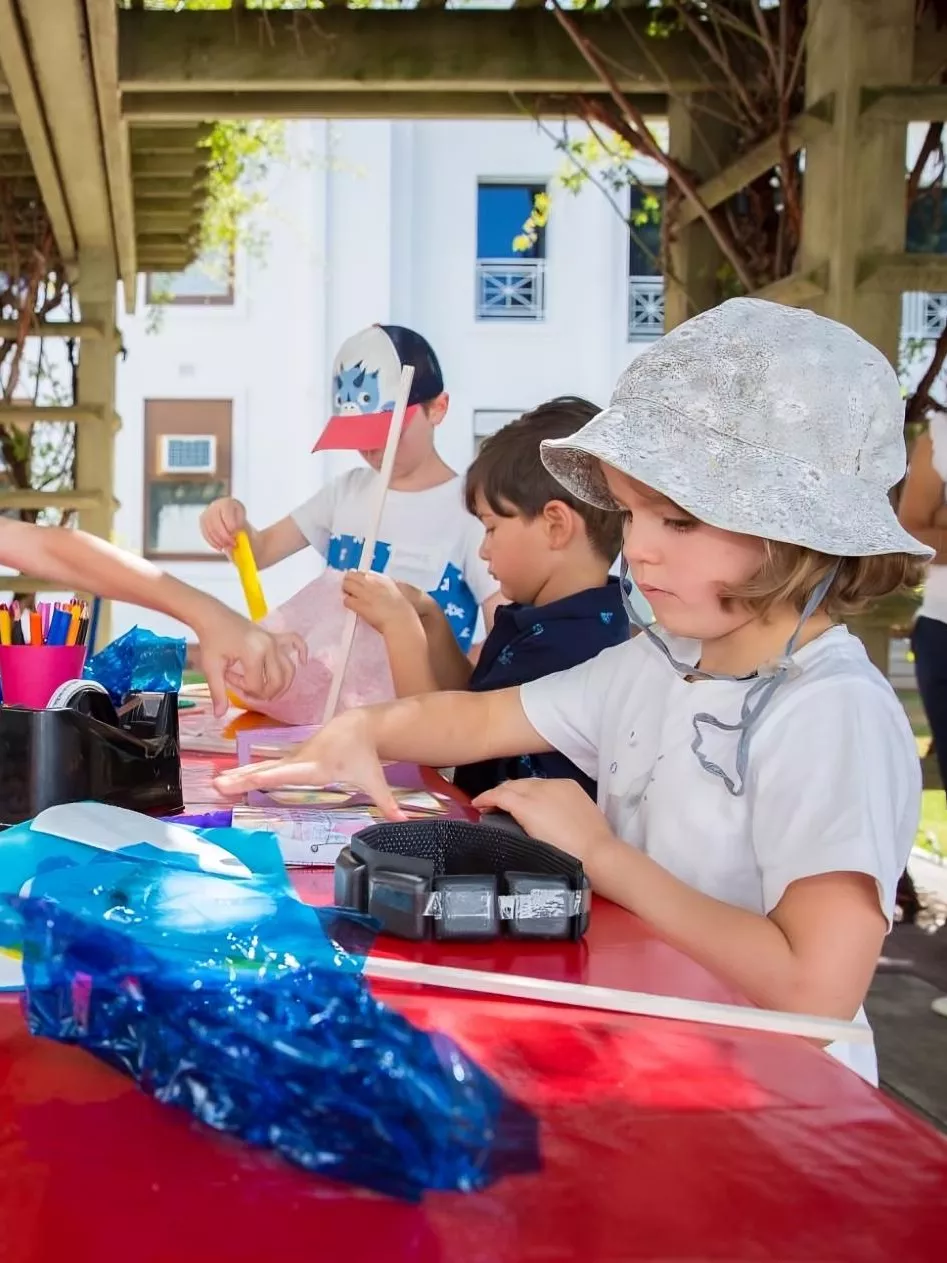 Four children stand around a table outdoors, each focusing on an idividual craft project. Four children stand around a table outdoors, each focusing on an idividual craft project.