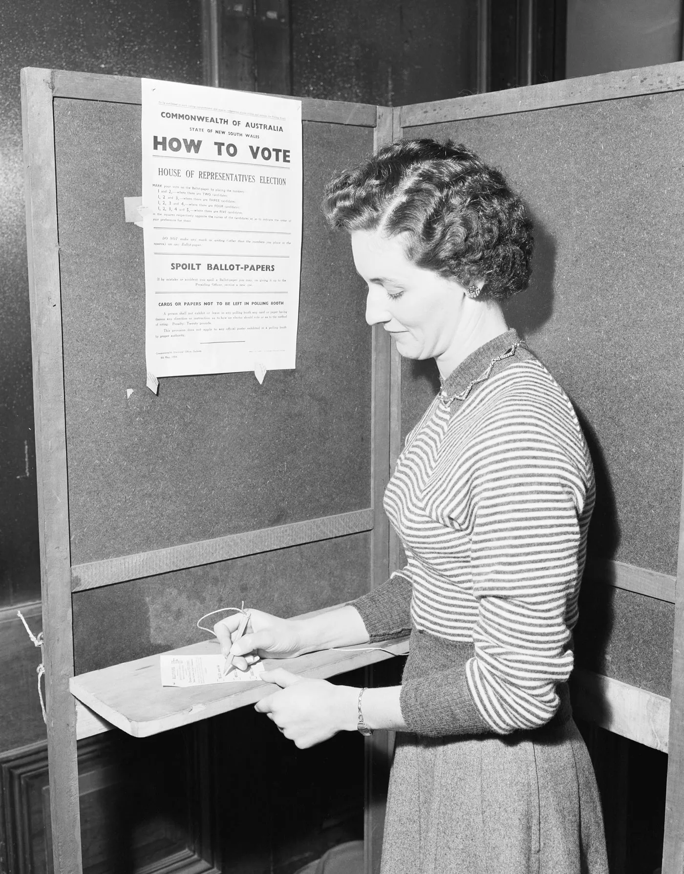 A woman voting in Australia in 1954.
Photograph Australian News & Information Services, photographer W (Bill) Brindle, NAA: A1200, L17064 A woman in a striped sweater stands in a polling booth holding a pencil above a voting card. A 'How to vote' instruction poster is pinned to the booth wall.